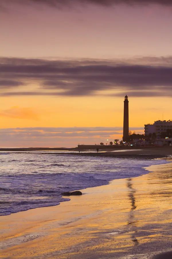 Atardecer en la playa y Faro de Maspalomas en Gran Canaria con reflejos dorados en la arena.